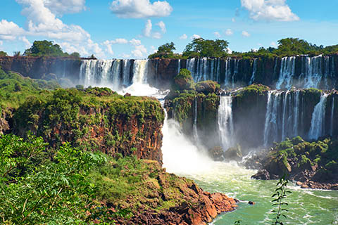 Waterfall in Argentina, water is spilling over the staggered rocky tops into a lush river below.