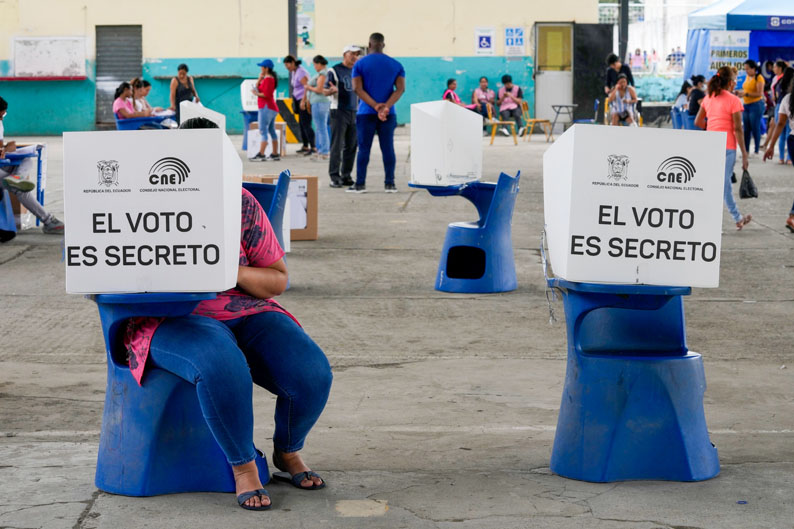 A person votes in a private voting booth in Ecuador. The booth's privacy screen says "El Voto es Secreto," meaning the Vote is Secret. 