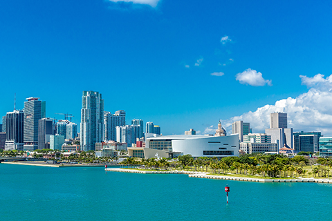 This is a photo from Shutterstock. It is the Miami skyline. This area of Miami represents the Brickell and Downtown neighborhoods. The picture was taken off of the bay. There are skyscrapers, the famous concert arena, and the blue ocean water which Miami is famous for.