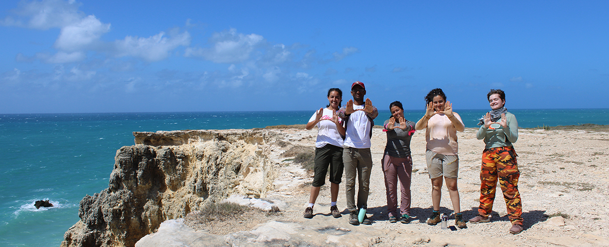 Group of students on a coastline making the U signs with their hands. 