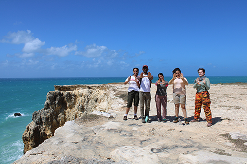 Group of students on a coastline making the U signs with their hands. 