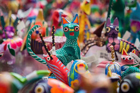 This is a stock photo from Shutterstock. Wood-carved animals are on display at a local market. The animals are all painted in vibrant colors. Each animal has a uniquely painted design on it.